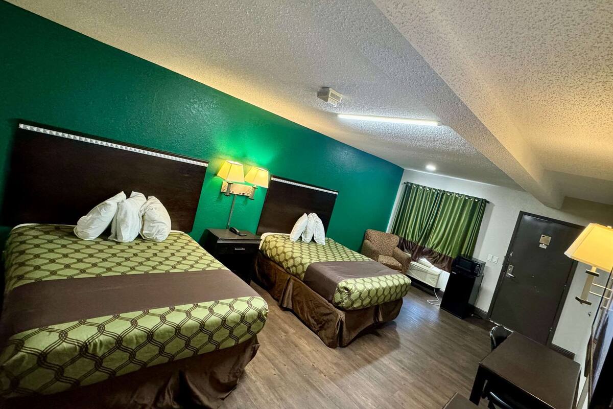 Ein Hotelzimmer mit zwei Betten, einem Schreibtisch, einem Stuhl, einem Kleiderschrank und einer Lampe.