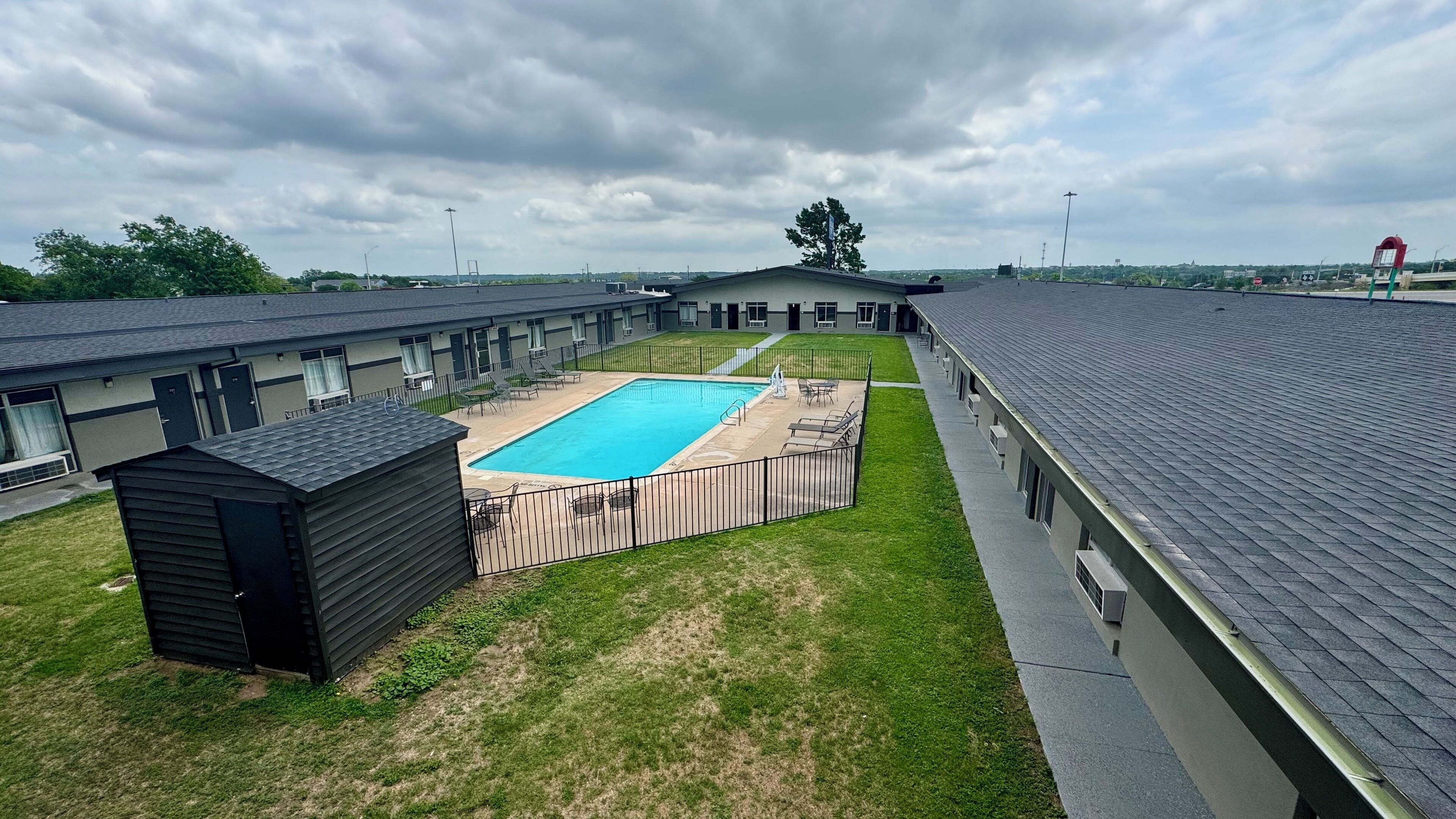 A motel with a swimming pool, a fenced yard, and a small shed.