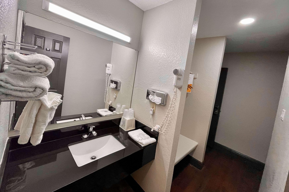 Ein Hotelbad mit einem schwarzen Waschbecken, einem Stapel weißer Handtücher und einem Spiegel.