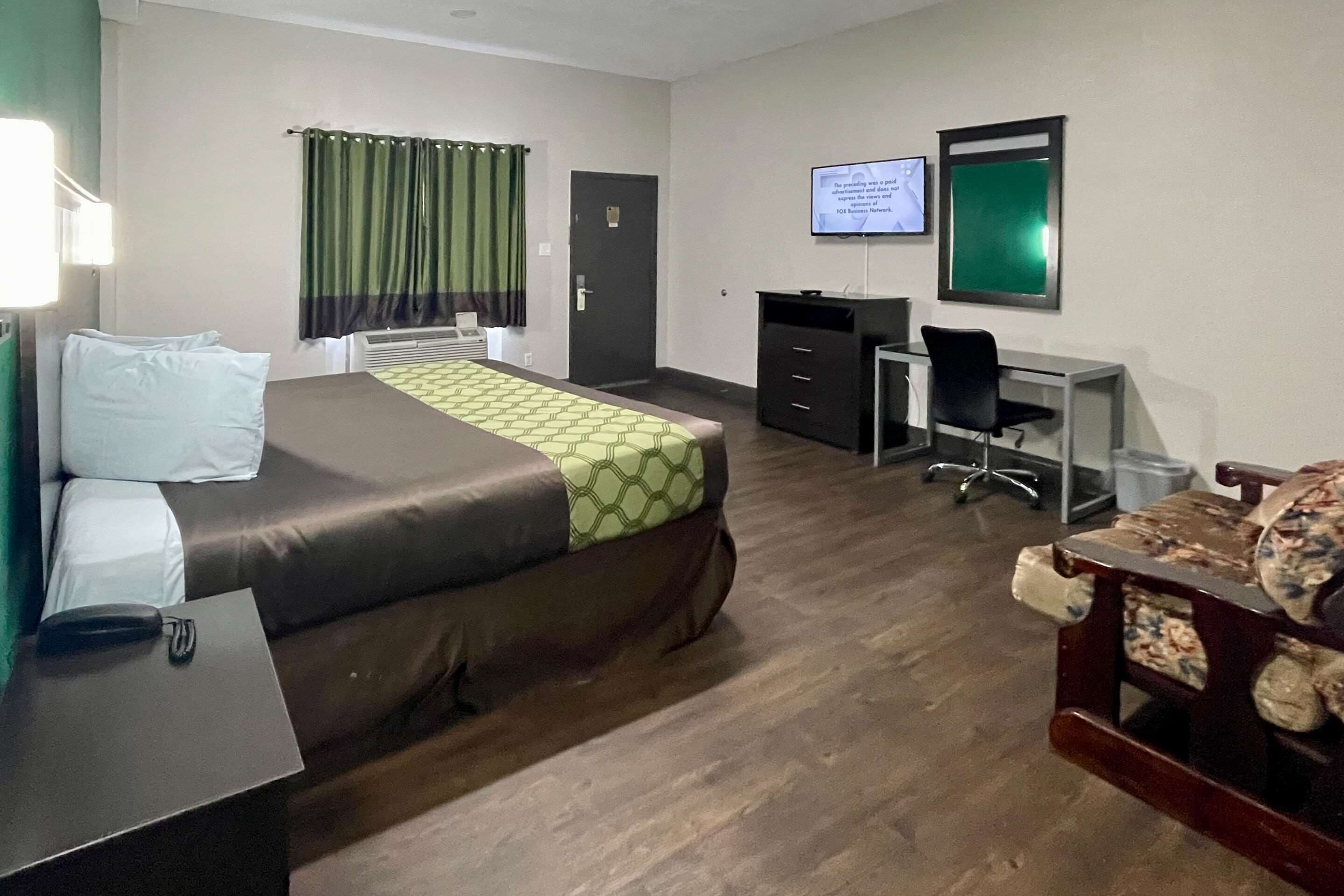 A hotel room with a bed, desk, chair, and a television on the wall.