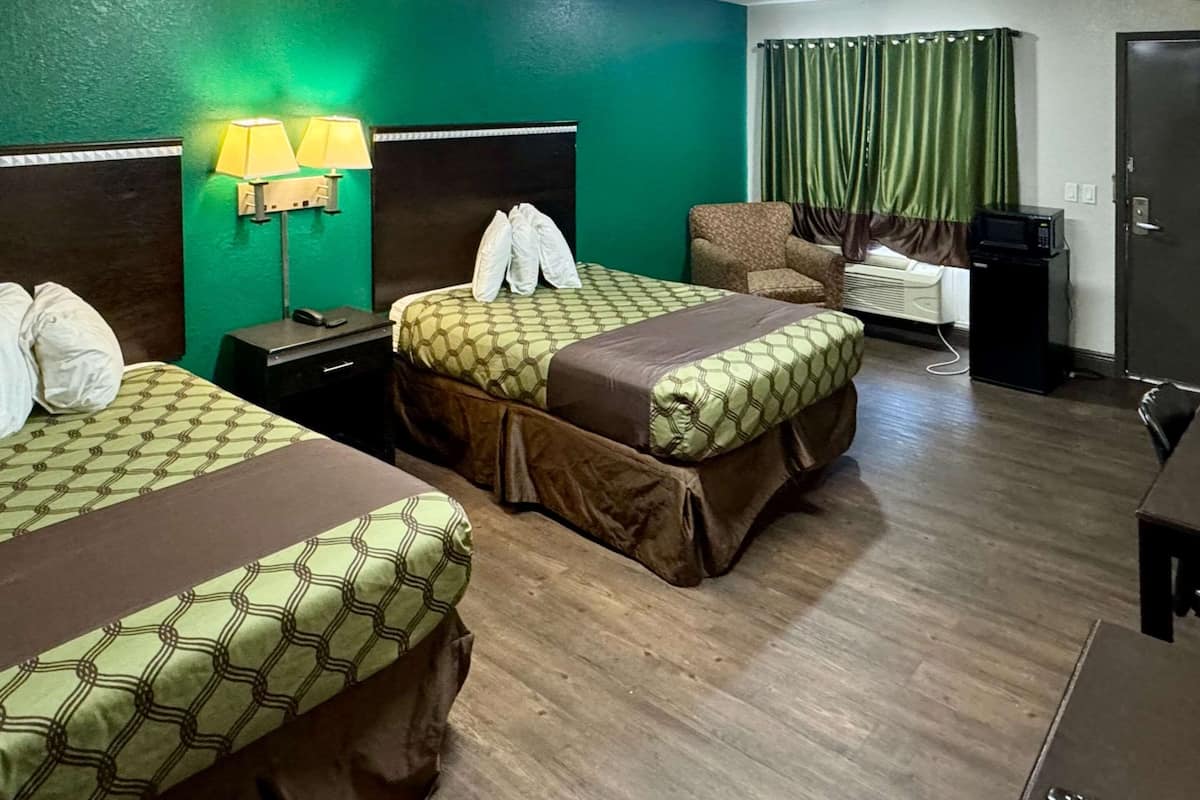 Ein Hotelzimmer mit zwei Betten, einem Sessel, einem Schreibtisch, einer Mikrowelle und einem Fernseher.