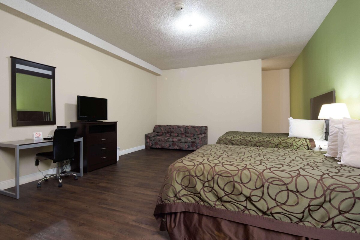 A hotel room with a bed, a desk with a computer, a chair, a sofa, and a lamp.