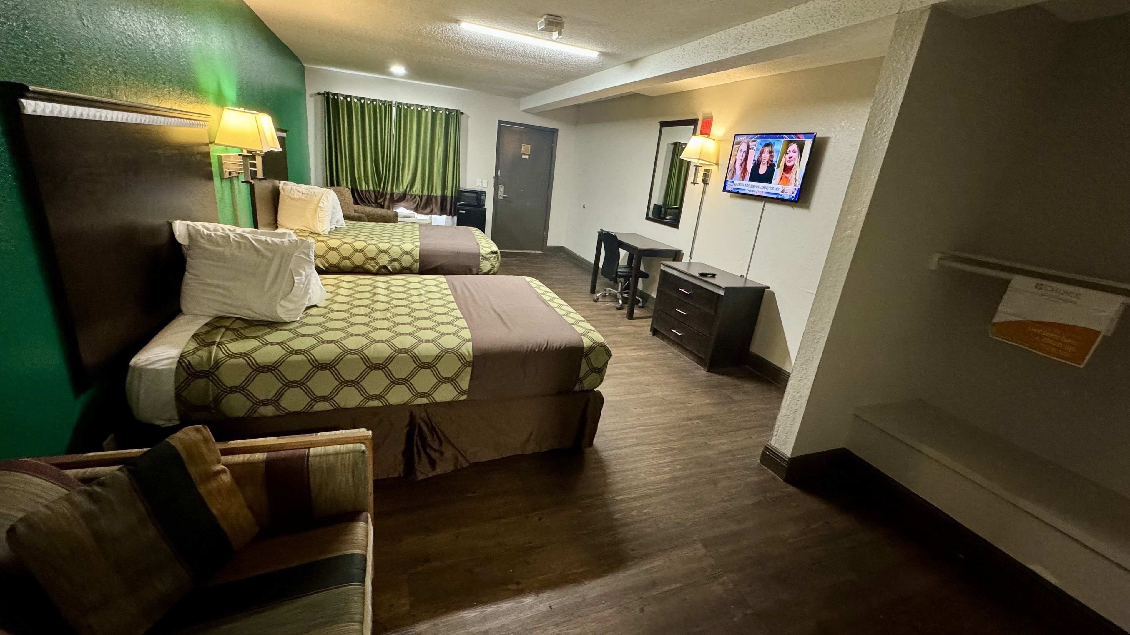 A hotel room with two beds, a desk, a chair, a TV, and a dresser.