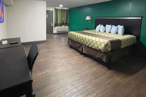 A hotel room with a bed, a desk, a chair, a lamp, and a bathroom visible through a door.