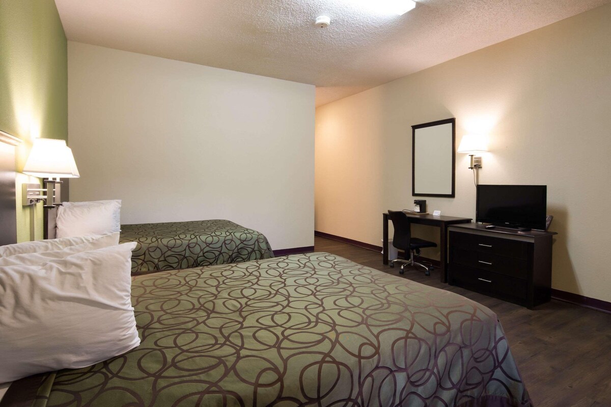 A hotel room with two beds, a desk with a chair, a television, and a mirror.