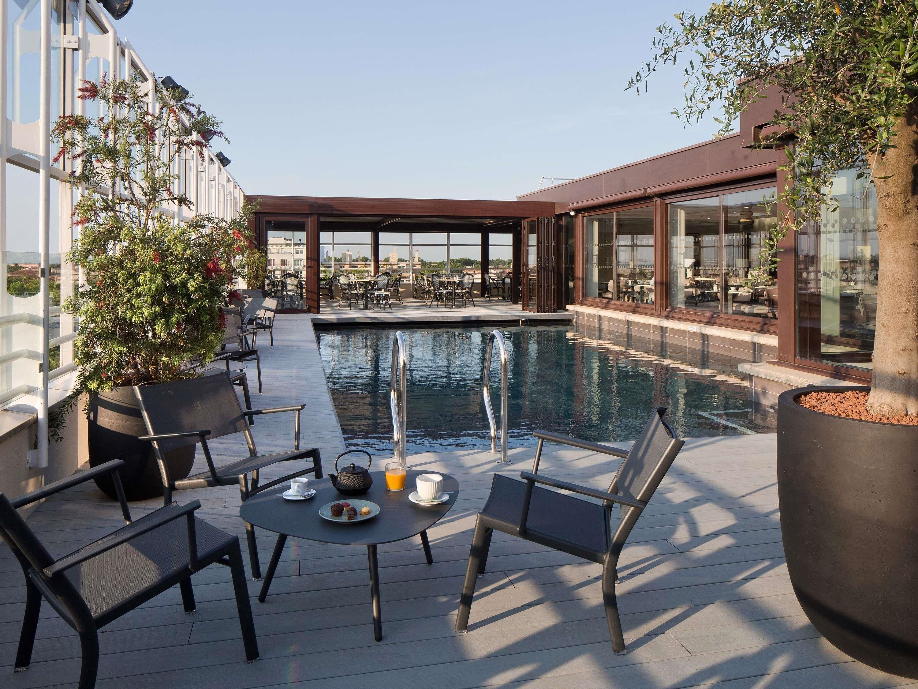 Un espace piscine aménagé sur le toit, avec des chaises longues, une table où sont servis des boissons et des collations, et une vue sur le paysage urbain.