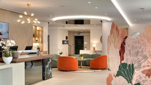 A modern hotel lobby with a reception desk, seating area, and a large decorative wall.