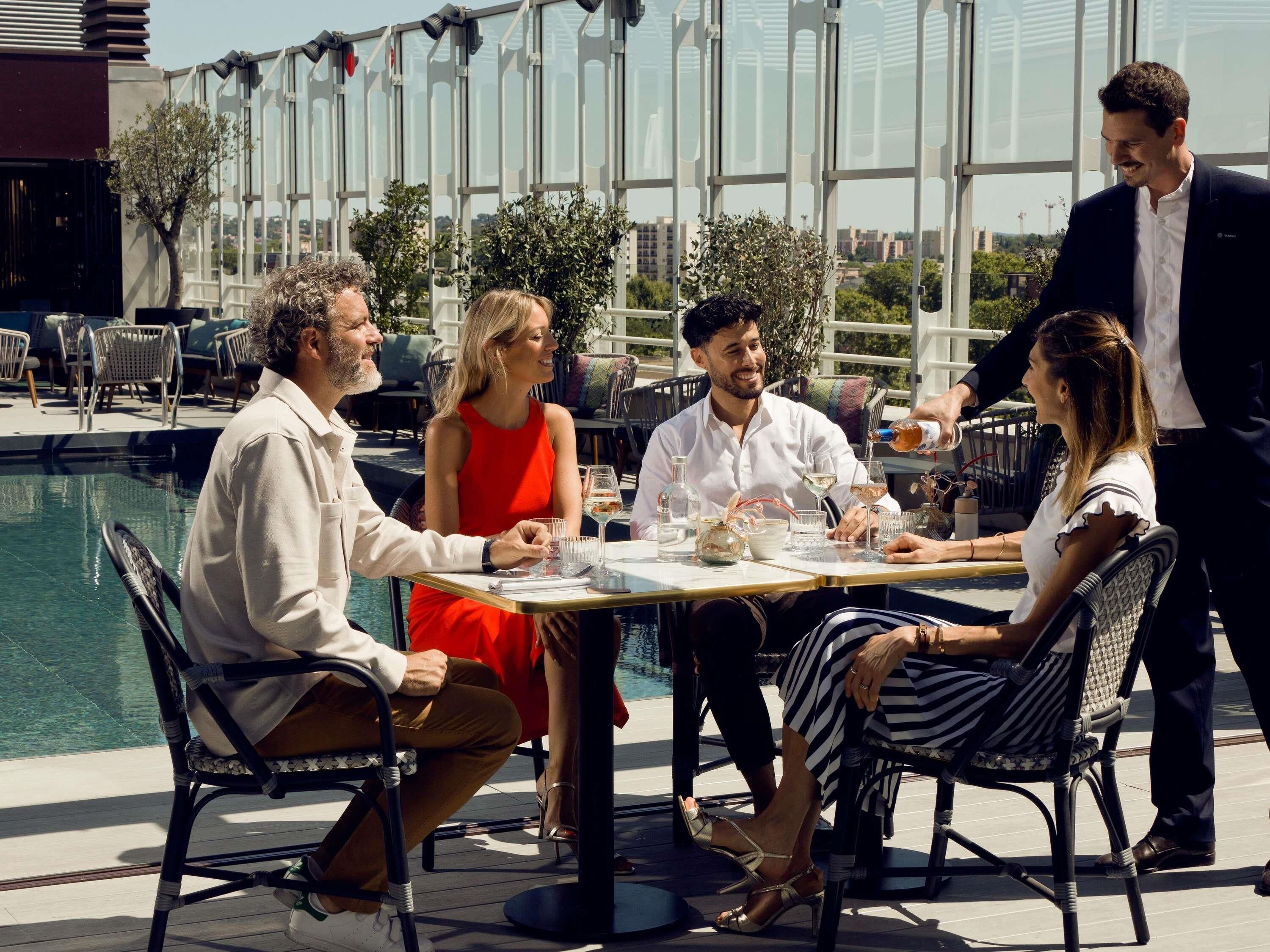 Un groupe de personnes est assis à une table en plein air, avec une piscine en arrière-plan.