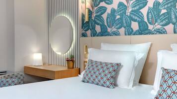 Une chambre d’hôtel comprenant un lit, une table de chevet, une lampe, un miroir et un mur orné d’un motif de feuilles.