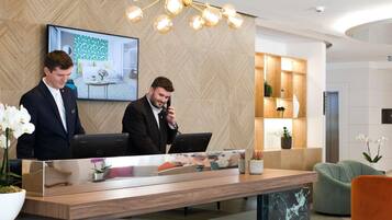 Um balcão de atendimento moderno com dois computadores, uma tela grande exibindo um quarto, e um elegante candelabro.