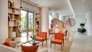 A modern living room with a sofa, two orange chairs, a coffee table, and a bookshelf filled with decorative items.