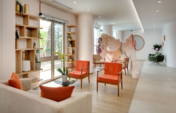 A modern living room with a sofa, two orange chairs, a coffee table, and a bookshelf filled with decorative items.