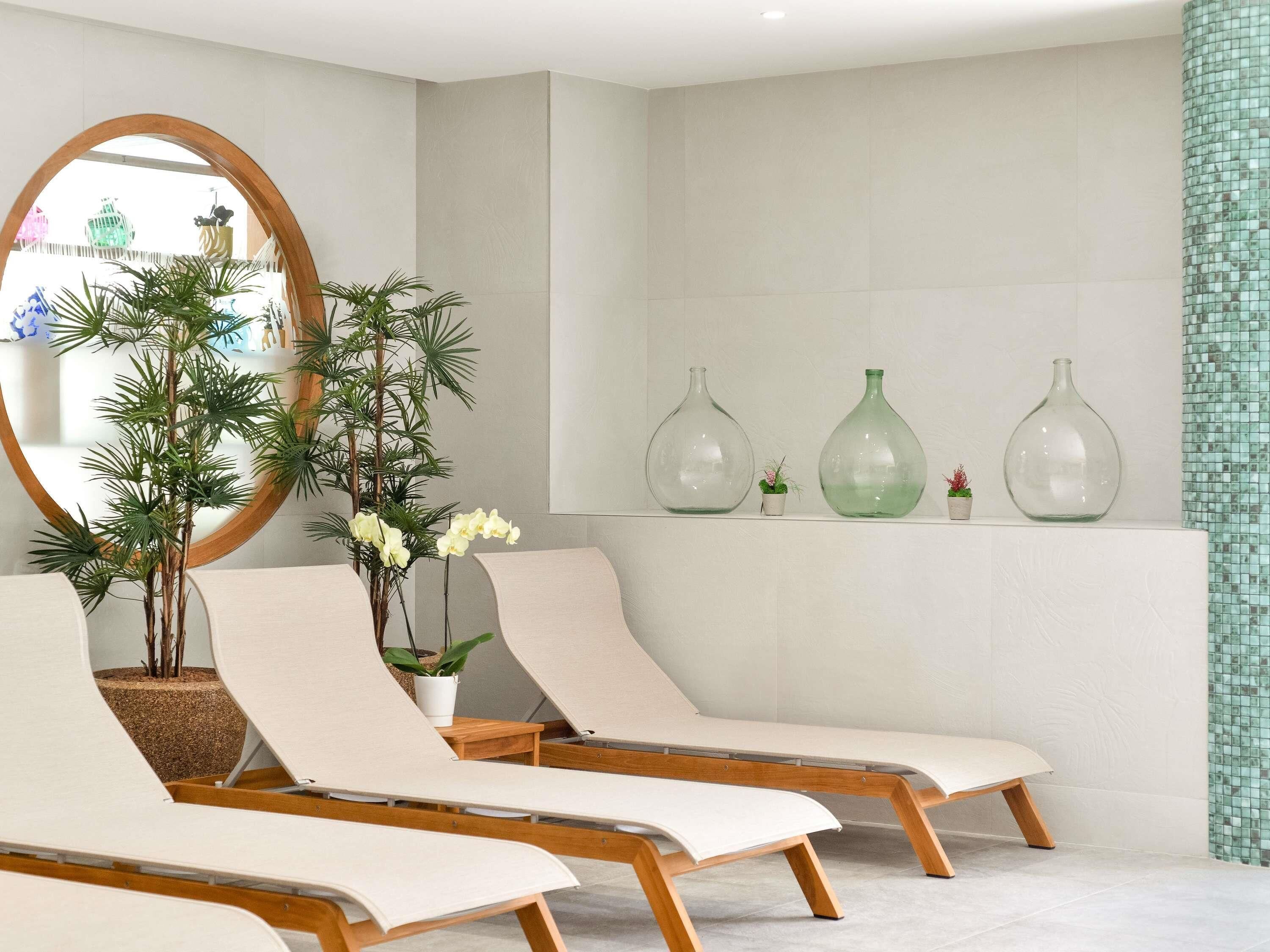 Een moderne spa ruimte met twee loungestoelen, een grote spiegel en decoratieve vazen op een plank.