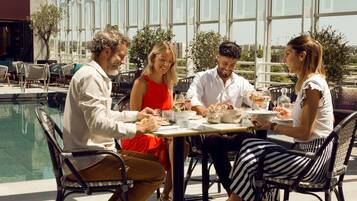 A group of people dining at an outdoor table with a pool in the background.
