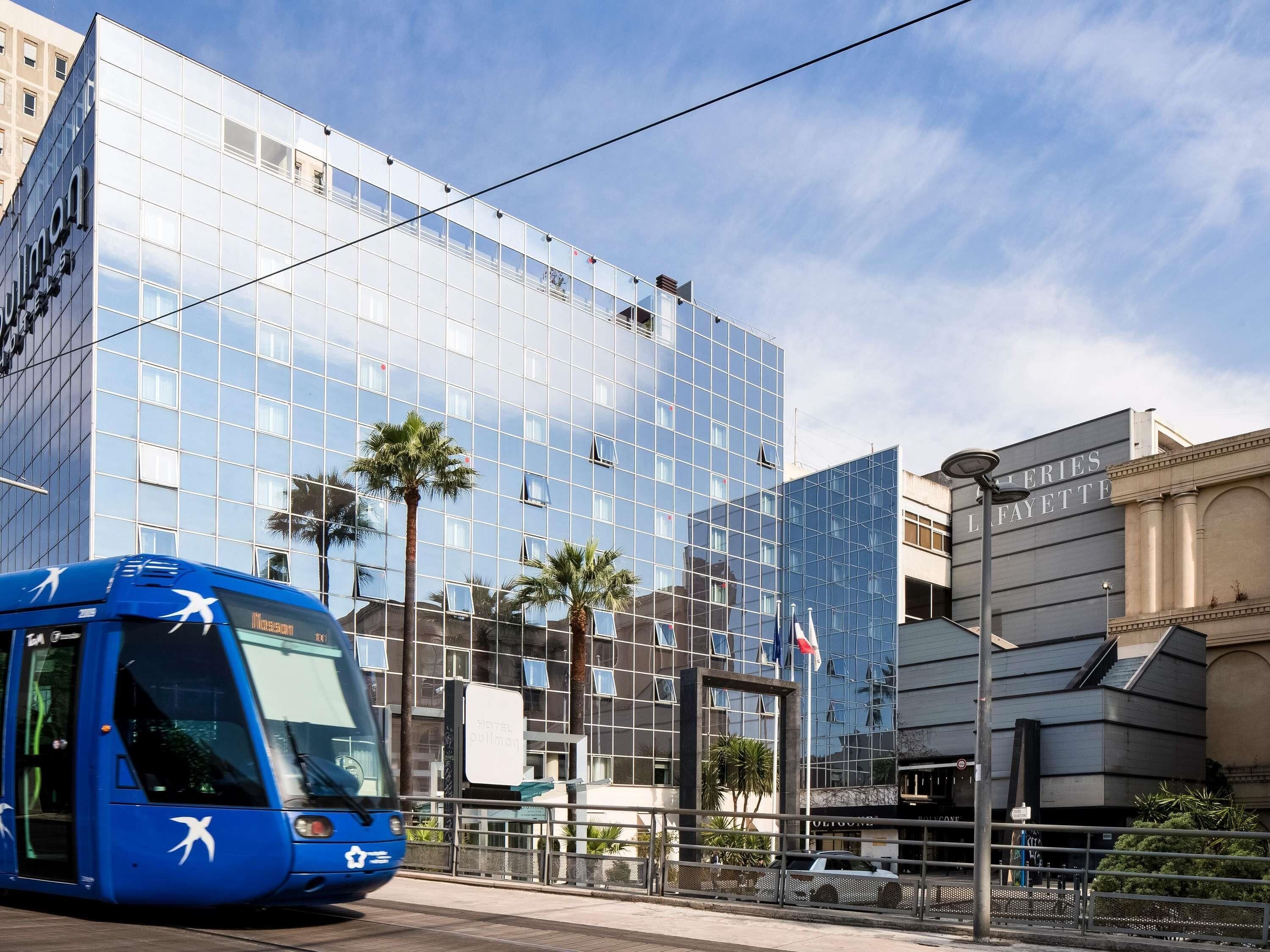 Een modern gebouw met een glazen gevel, een blauwe bus ervoor en een bordje met 'L'AFAYETTE' aan de rechterkant.