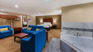 A hotel room with a bed, two blue sofas, a small table, a bathroom with a bathtub, and a mirror. - Quality Inn Marysville (Marysville)