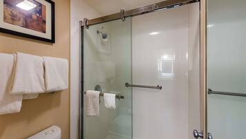 A glass-enclosed shower with a towel rack, a framed picture on the wall, and a toilet with a visible flush handle.