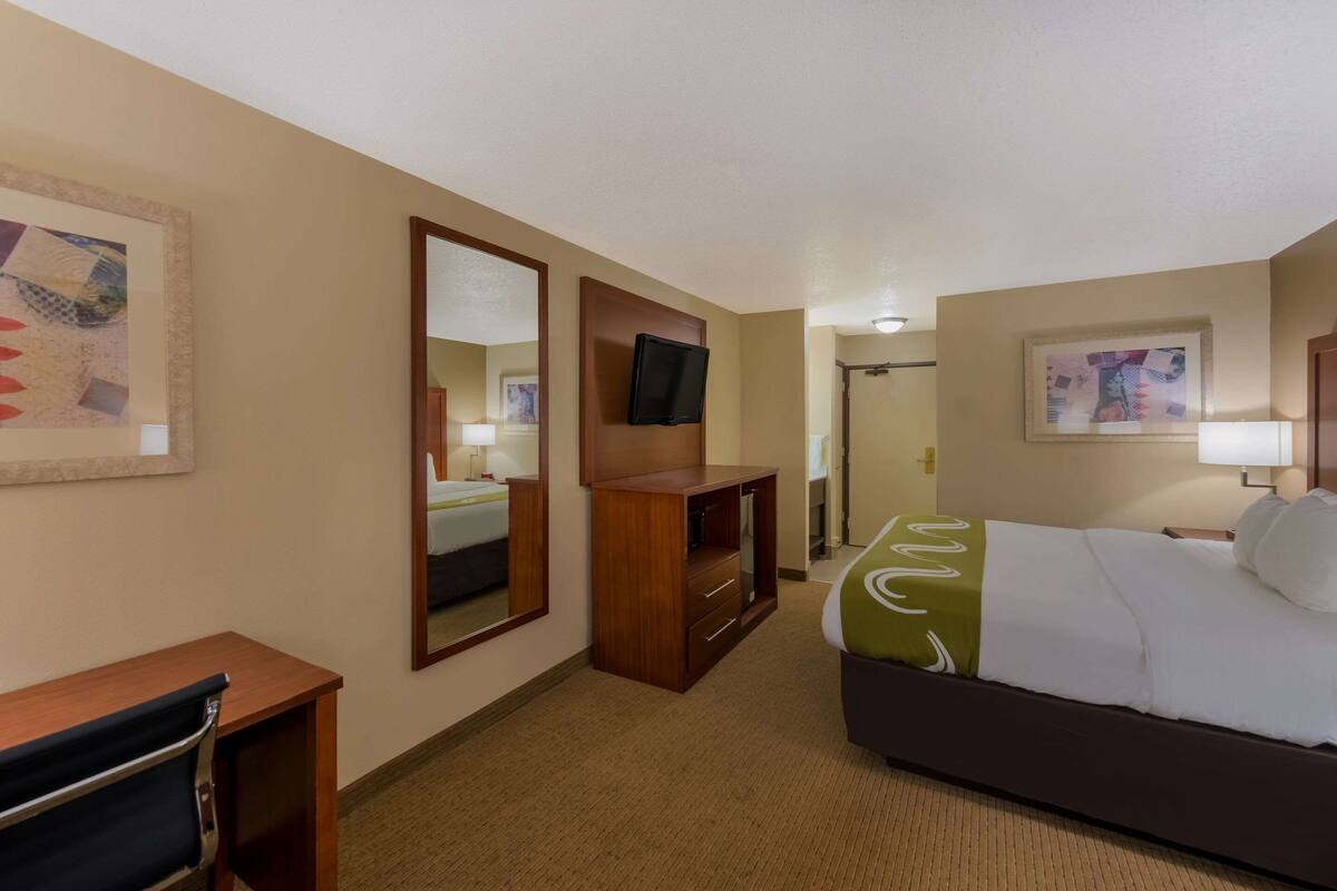 A hotel room with a bed, a desk, a chair, a TV, and a mirror.