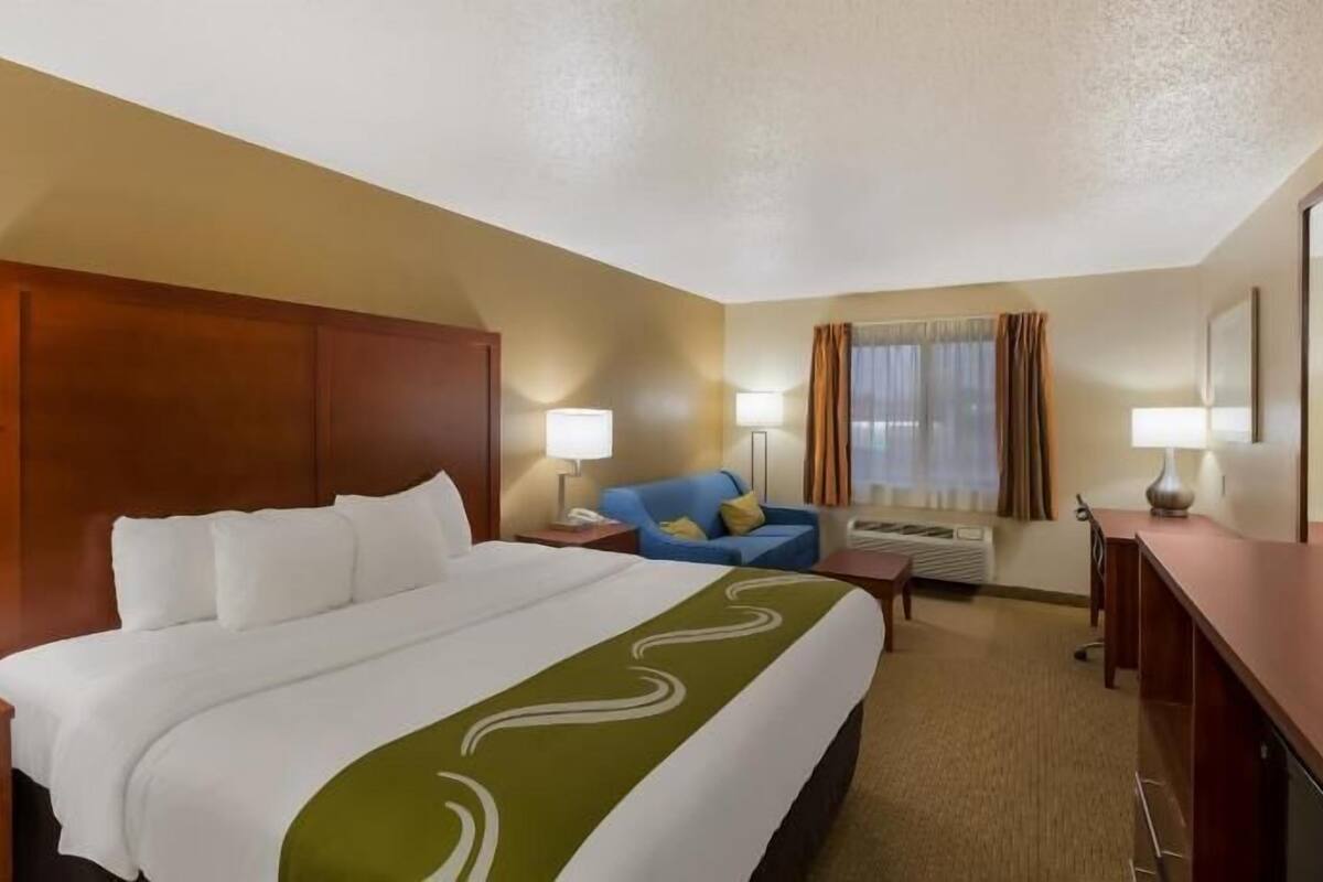 A hotel room with a large bed, a blue armchair, a desk, and a television.