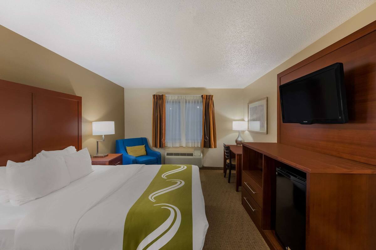 A hotel room with a large bed, a desk with a television, a chair, and a window with curtains.
