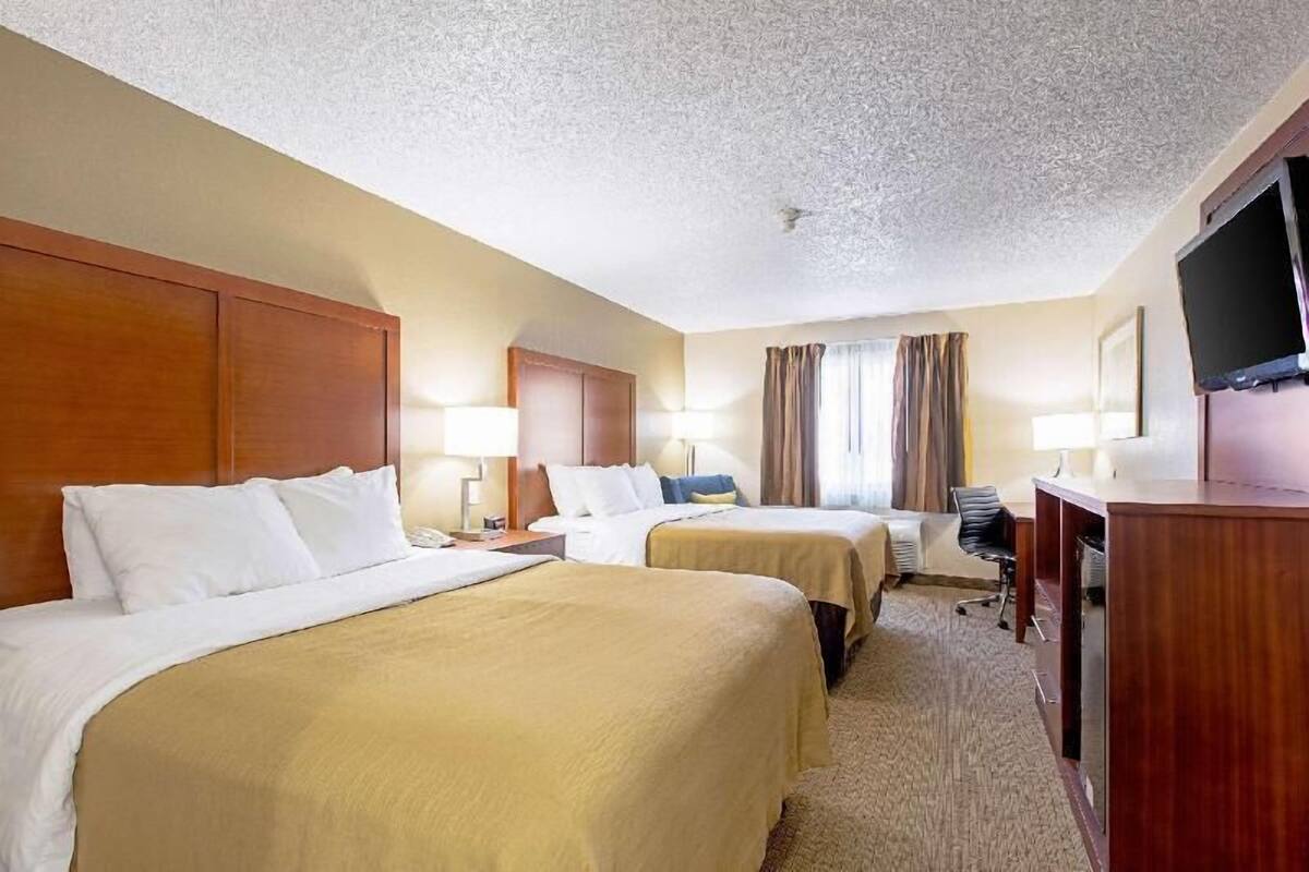 A hotel room with two beds, a desk, a chair, a television, and a window with curtains.