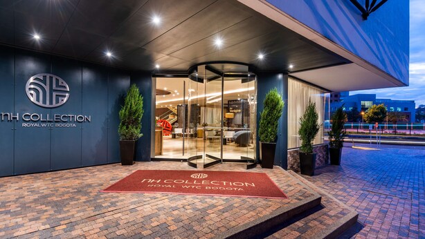 A hotel entrance with a glass door, a red carpet, and a logo on the wall. - NH Collection Bogotá WTC Royal (Bogotá)