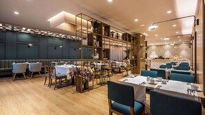 A modern restaurant with wooden floors, blue upholstered chairs, and a central bar area. - NH Collection Bogotá WTC Royal (Bogotá)