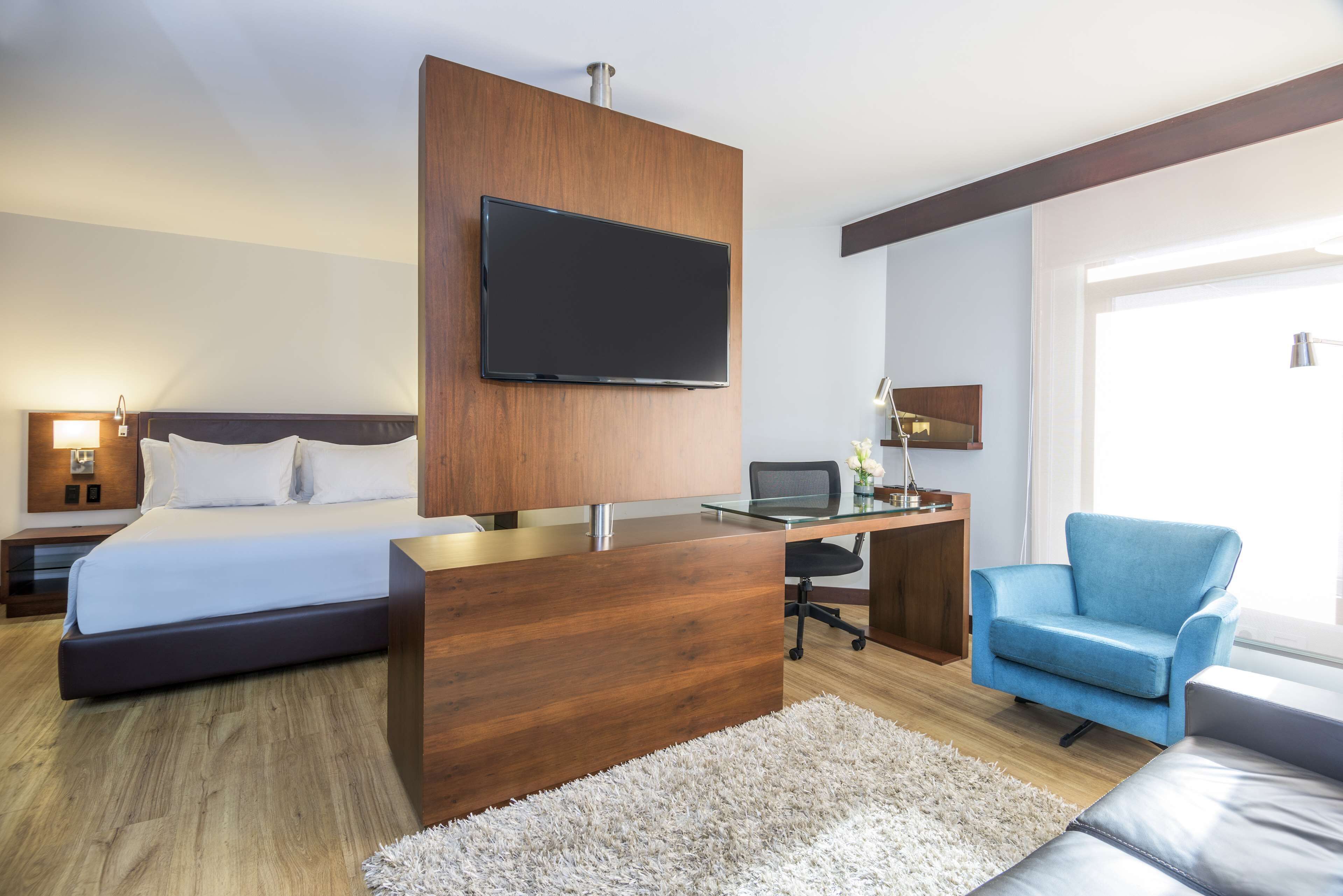 Une chambre d’hôtel moderne avec un grand lit, un bureau, un téléviseur à écran plat et un fauteuil bleu.