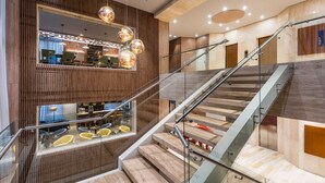 A modern interior with a glass railing staircase, wooden paneling, and contemporary lighting fixtures. - NH Collection Bogotá WTC Royal (Bogotá)