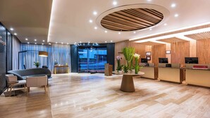 A modern hotel lobby with a reception desk, seating area, and a large window. - NH Collection Bogotá WTC Royal (Bogotá)
