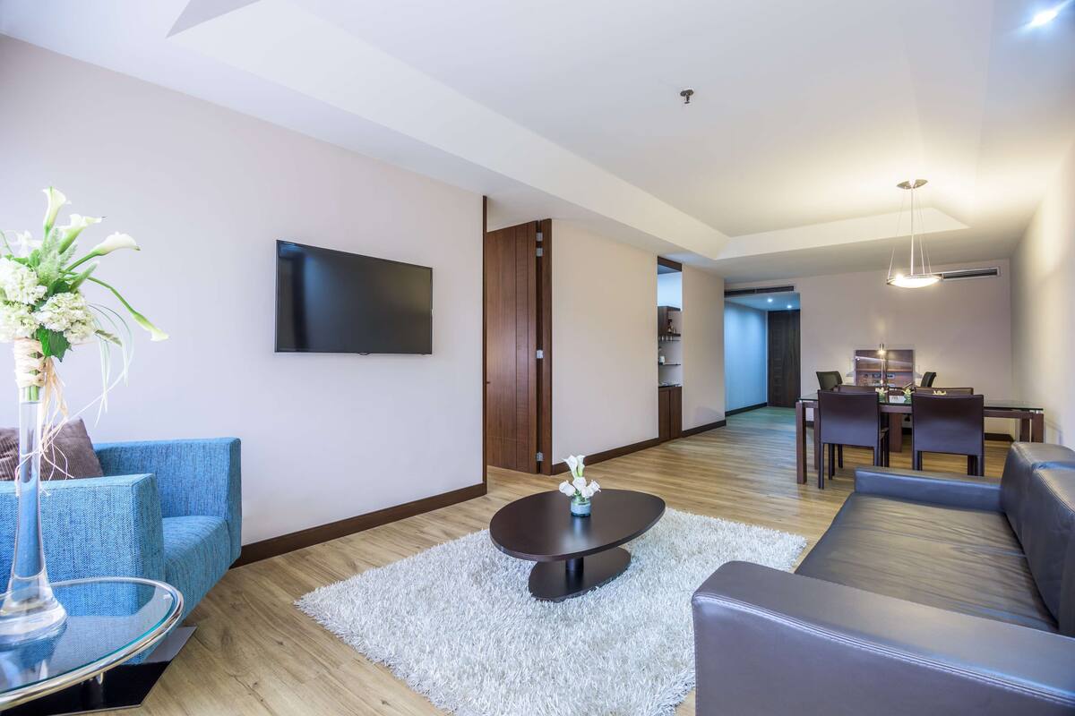 A modern living room with a sofa, a coffee table, a TV, and a dining area with chairs and a table.