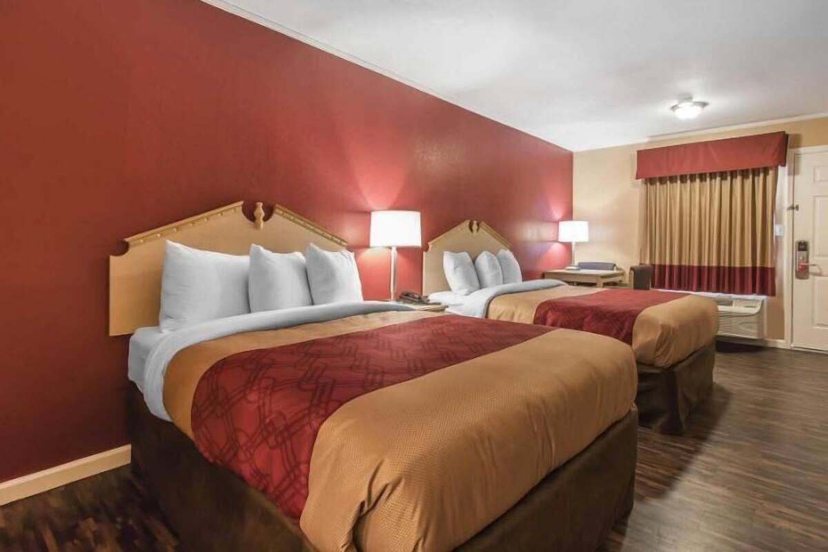 A hotel room with two beds, red walls, and a wooden headboard.