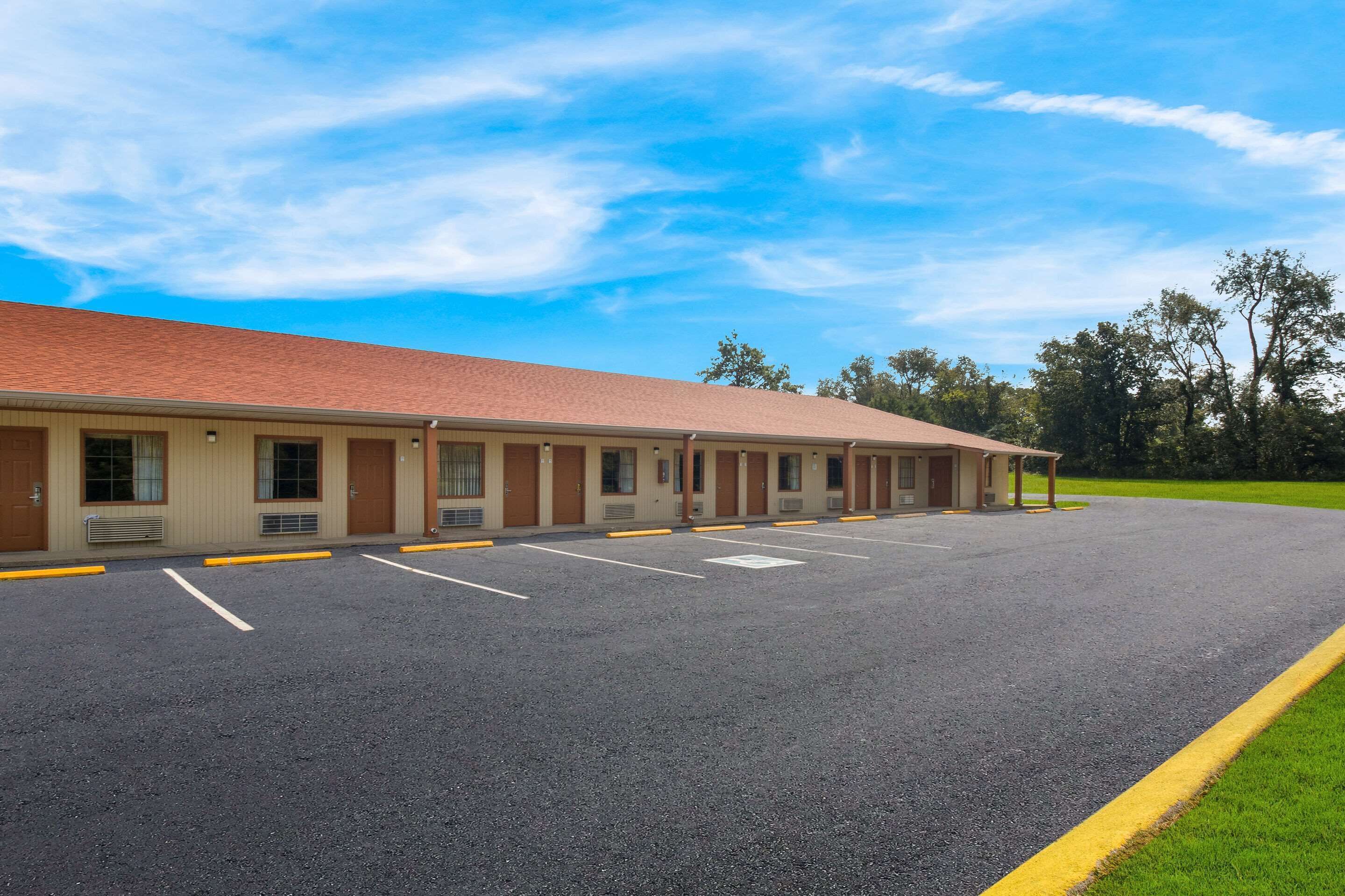 Un motel con una hilera de habitaciones, estacionamiento y un área verde.