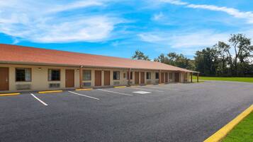 Un motel con una hilera de habitaciones, estacionamiento y un área verde.