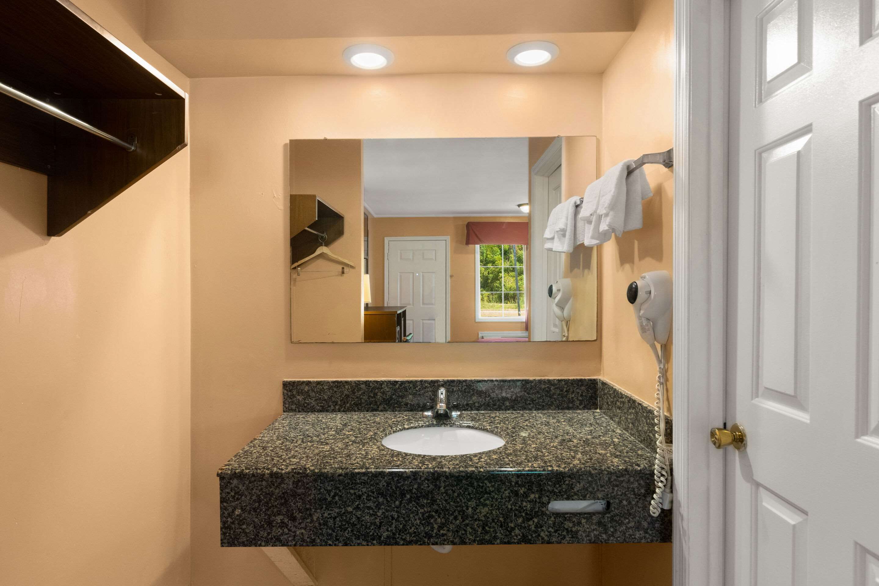 A bathroom with a granite countertop sink, a mirror above it, and a towel rack.