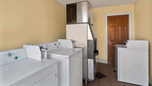 A laundry room with a front-loading washer, a stacked dryer, and a wall-mounted vent. - Econo Lodge Cornersville I-65 (Cornersville)