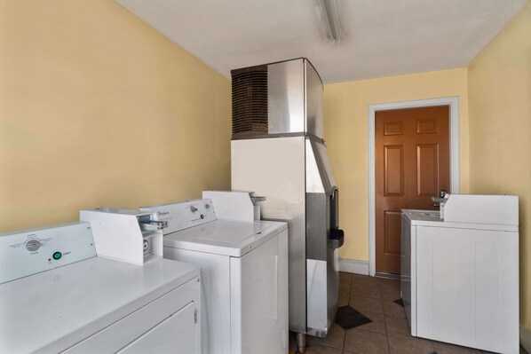A laundry room with a front-loading washer, a stacked dryer, and a wall-mounted vent.