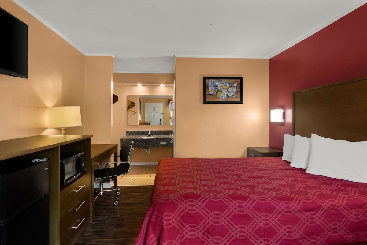 A hotel room with a bed, a desk with a lamp, a microwave, and a refrigerator.