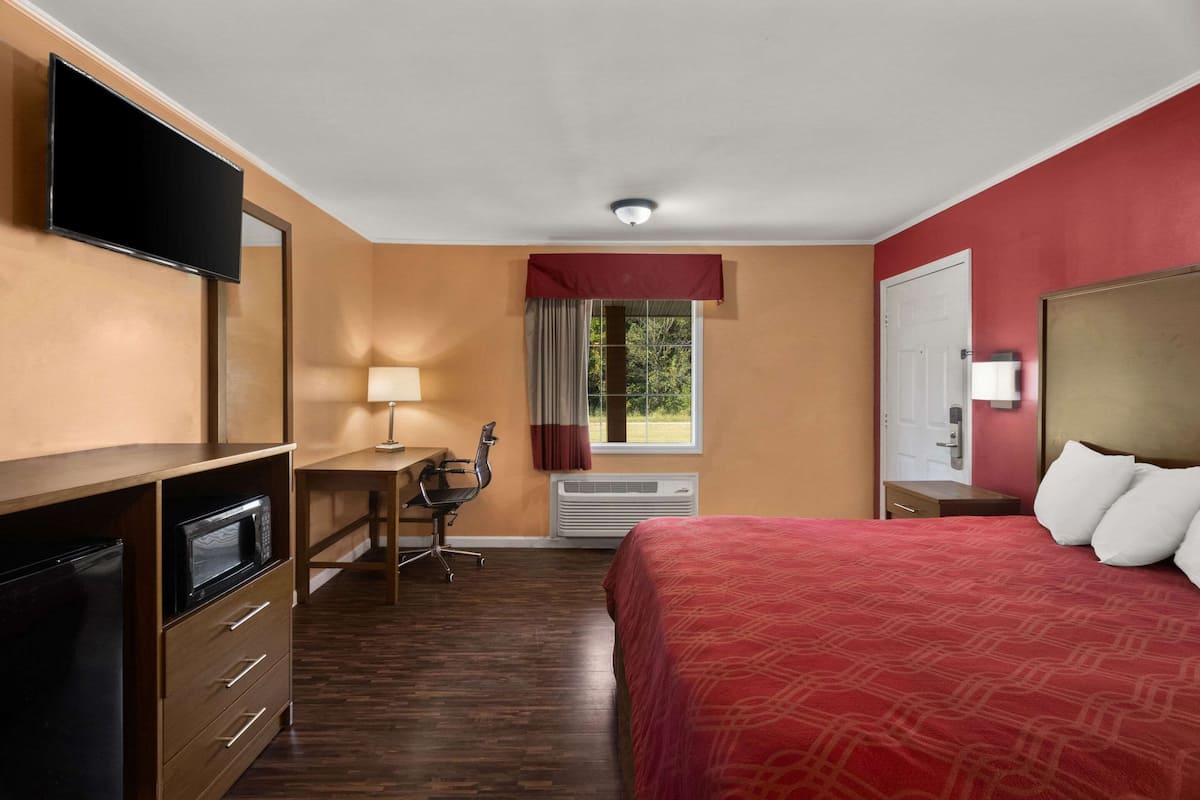 A hotel room with a bed, a desk, a chair, a television, and a window with curtains.