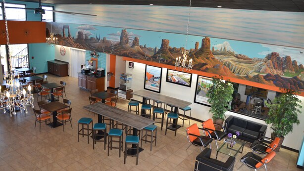Un restaurante amplio con mesas y sillas altas, una zona de bar y un mural de paisaje desértico en la pared.