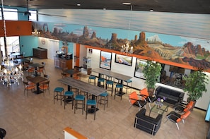 Un restaurante amplio con mesas y sillas altas, una zona de bar y un mural de paisaje desértico en la pared.