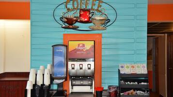 A coffee station with a coffee machine, cups, and a sign that reads "Coffee".