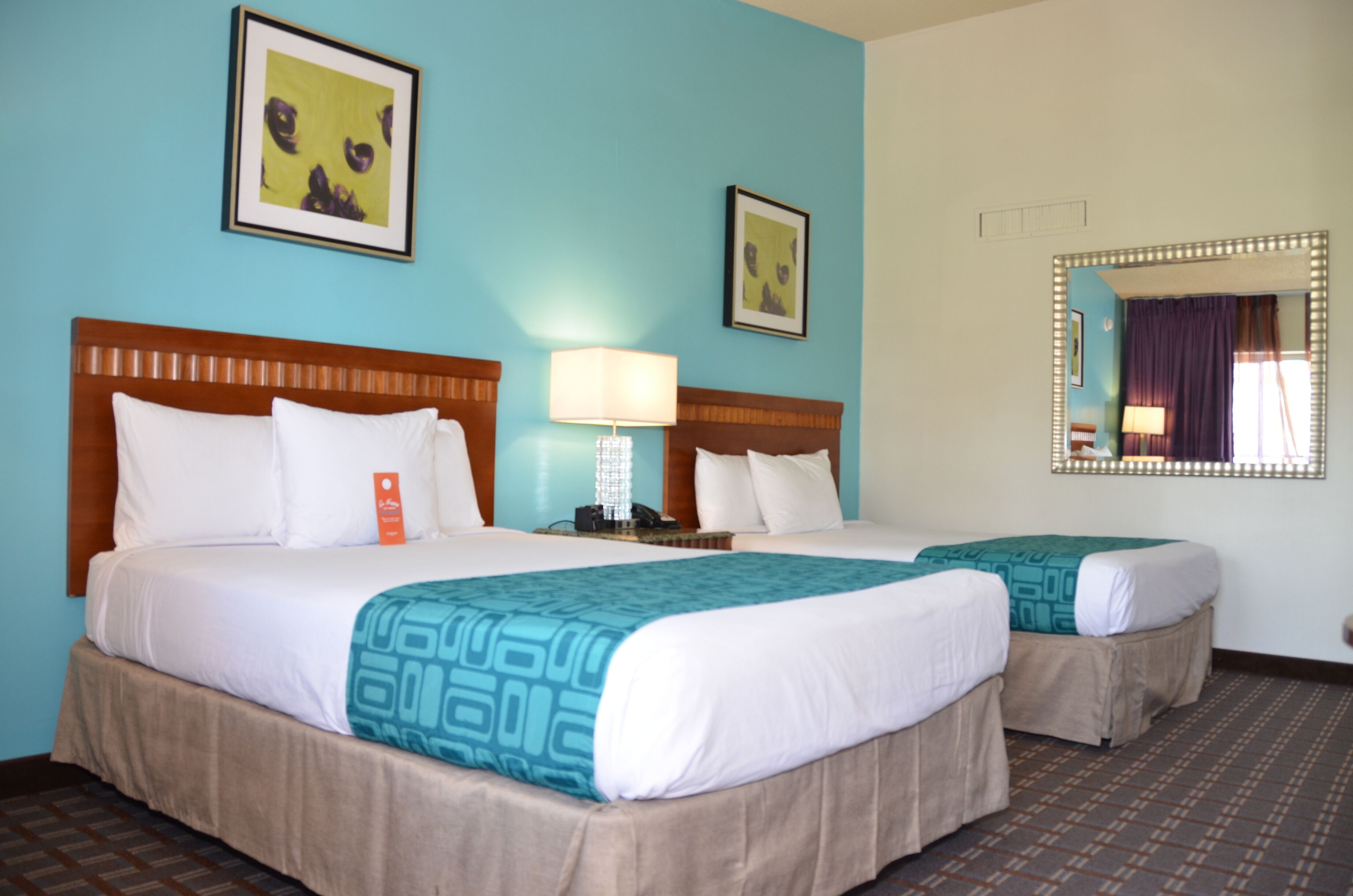 A hotel room with two beds, a nightstand, a lamp, and framed artwork on the walls.