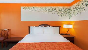 A hotel room with a bed, a nightstand, a chair, and a wall with a bamboo leaf mural.