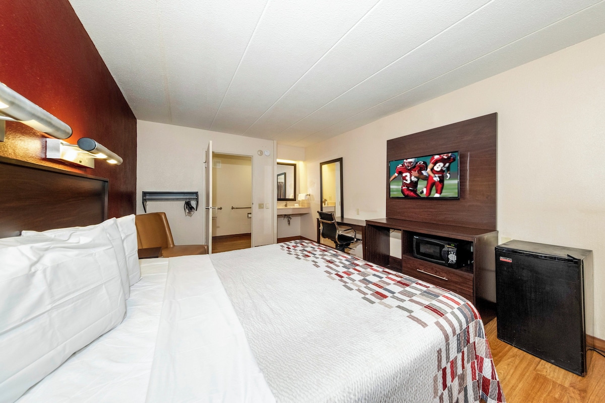 A hotel room with a bed, a desk, a chair, a television, and a refrigerator.