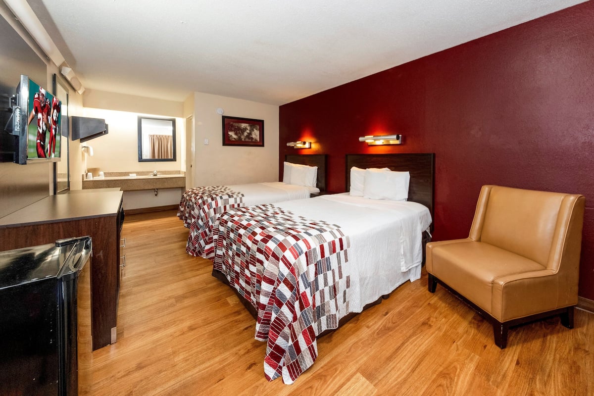 A hotel room with two beds, a desk, a chair, and a television.