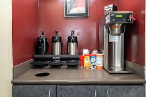 Een kitchenette met een koffiezetapparaat, twee thermosflessen en drie melkpakken voor koffie.