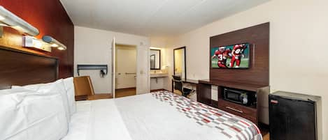 Habitación de hotel con una cama, un escritorio, un televisor y un microondas.