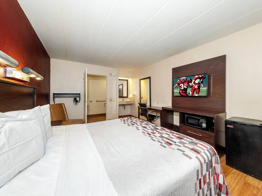 Habitación de hotel con una cama, un escritorio, un televisor y un microondas.