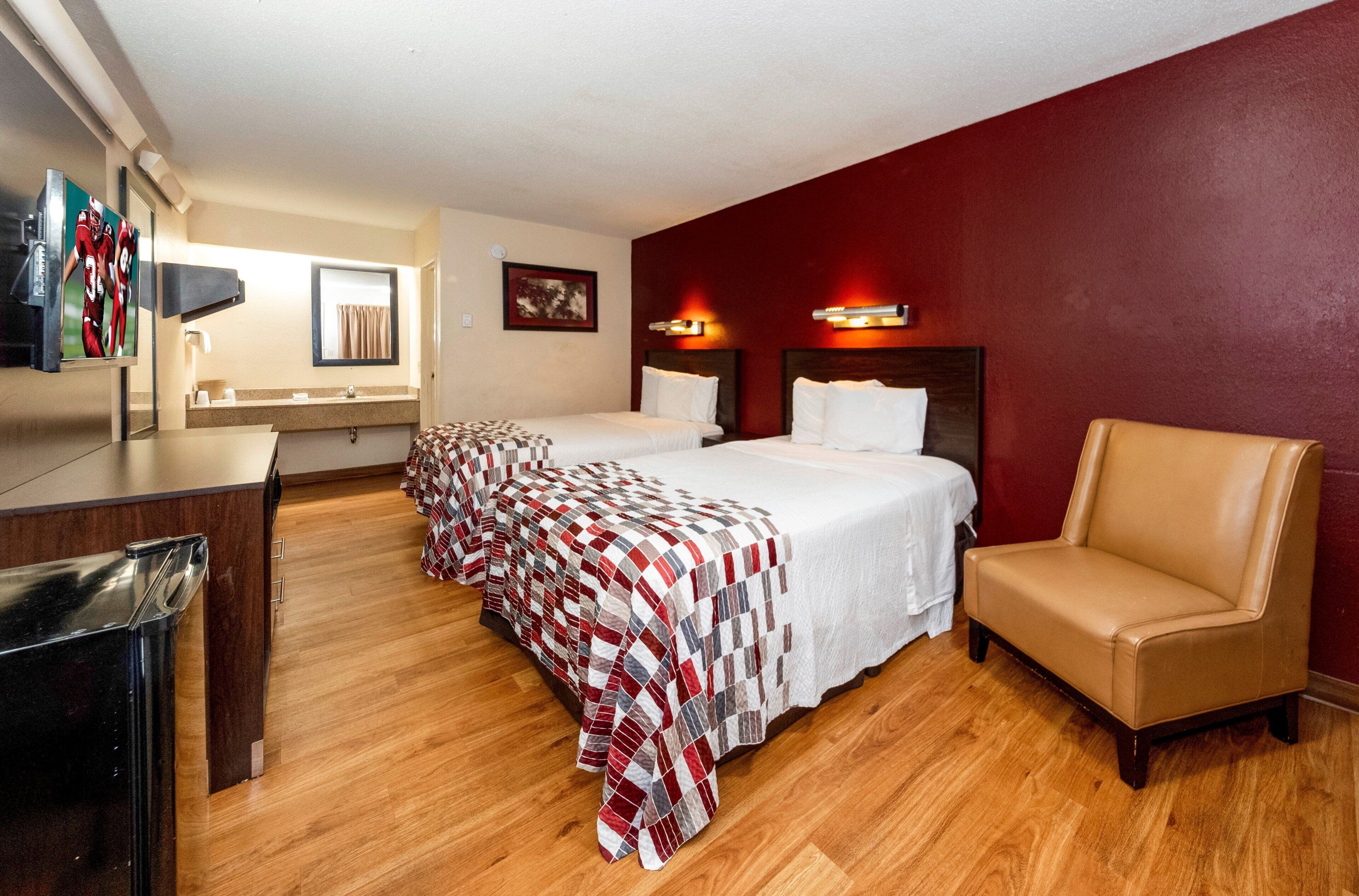 A hotel room with two beds, a desk, a chair, and a television.
